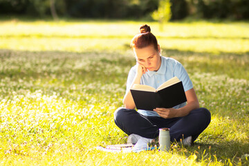 pensive, bored woman sits and rests on green grass. Serious student girl in the park, reading a book, studies. outside