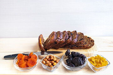 Dried apricots, raisins, prunes, hazelnuts and cut rye bread with dried fruits on a light wooden surface.
