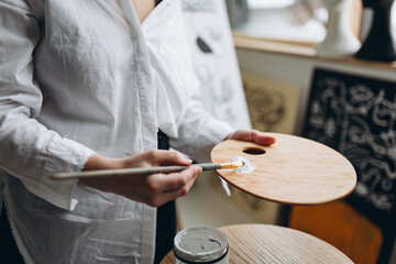 Woman mixing white paint on wooden art palette