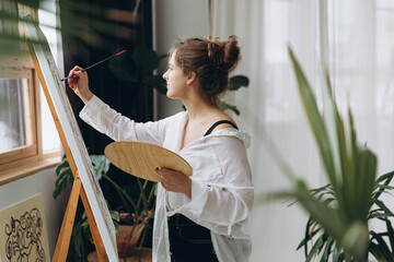 Side view of young woman painting on canvas with brush