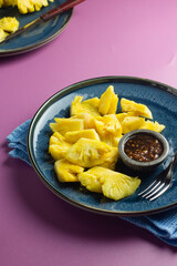 Rujak Nanas or Indonesian pineapple salad served with peanut chili sauce with palm sugar. blue ceramic plate on purple isolated background. 