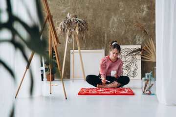 Inspired woman painting on canvas while sitting on floor