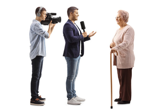 Full Length Profile Shot Of A Male Reporter With A Microphone And A Cameraman Interviewing An Elderly Woman