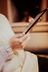 Woman in white reading interesting e-book reader while sitting near fireplace at home. Cozy winter pic of lady relaxing alone with novel.