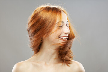 Beautiful red hair girl posing with waving hair. Studio portrait on gray background