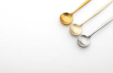 Different color metal spoons on a white table, silverware, copy space