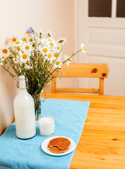 Simply stylish wooden kitchen with bottle of milk and glass on table, summer flowers camomile, healthy foog moring concept close up