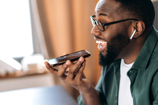 Happy Smiling Black Guy, Holding And Using Cell Phone, Speaking With Friend Or Colleague Speakerphone, Sitting At Home Or Office, Record Voice Message