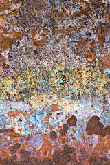Paint flaking away from colorful wall,  many layers of old paint and base material (portland concrete), vertical full frame with large empty copy space.