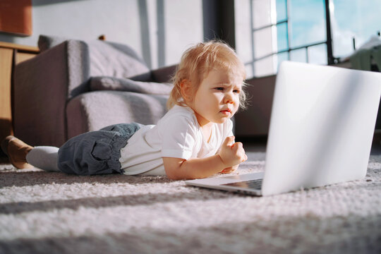 Happy childhood and youth. Favorite children's TV show cartoons. The girl's daughter looks at the laptop monitor. posing in a photo studio smiling. Little baby girl blonde with blue eyes.