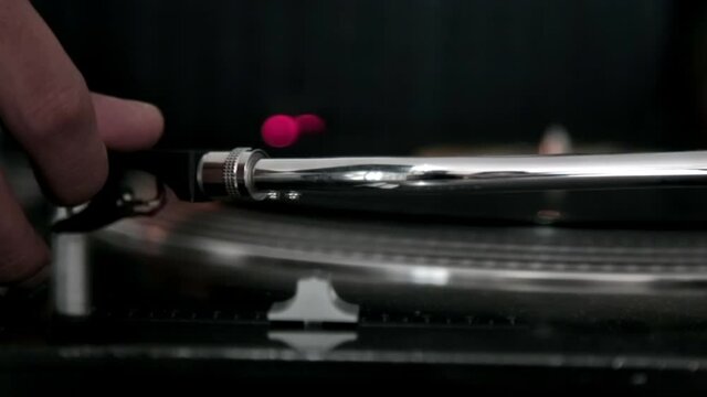 Hand holding the turntable needle with a spinning vinyl record behind it