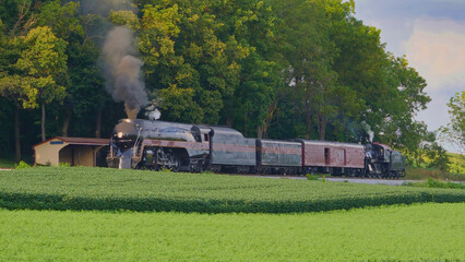 View of An Antique Restored Steam Locomotive Blowing Smoke and Steam Traveling Thru Farmlands and Countryside on a Sunny Summer Day