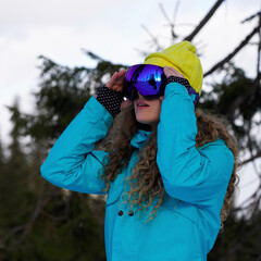 Fototapeta na wymiar Beautiful curly girl in bright snowboard clothes wears mirrored blue goggles for riding on a sunny day. ski vacation