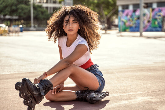 Young fit black woman on roller skates relaxing after riding outdoors on urban street.