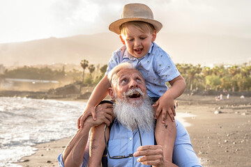 Happy kid playing on the beach with his grandfather, celebrating grandfather's day together, smiling, having fun.