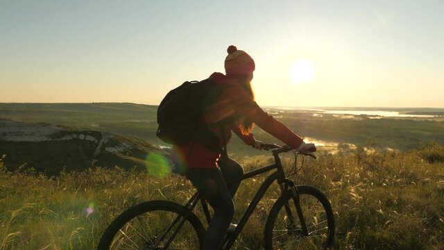 Woman of a cyclist traveler rides along the edge of the mountain, admiring the landscape and the sunrise. Free tourist rides a bike in nature in sun. Sports lifestyle. Cyclist exercising