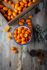 Top view of fresh kumquats in the plate on the natural wooden background. Cumquat or kumquat.
