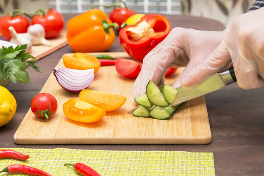 Chef cutting cucumber and different vegetables for salad close up. Hands in gloves cooking healthy vegetarian vegan diet food	
