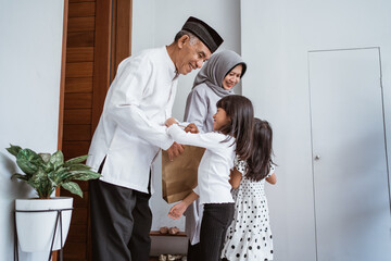 happy asian family giving present to their muslim grandparents during eid mubarak celebration. suprise gift to family