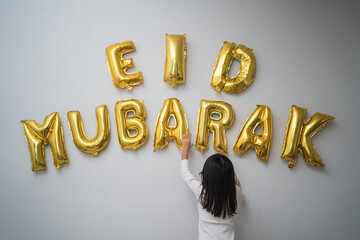 portrait kid muslim decorating eid mubarak letter made of baloon decoration against the wall at home