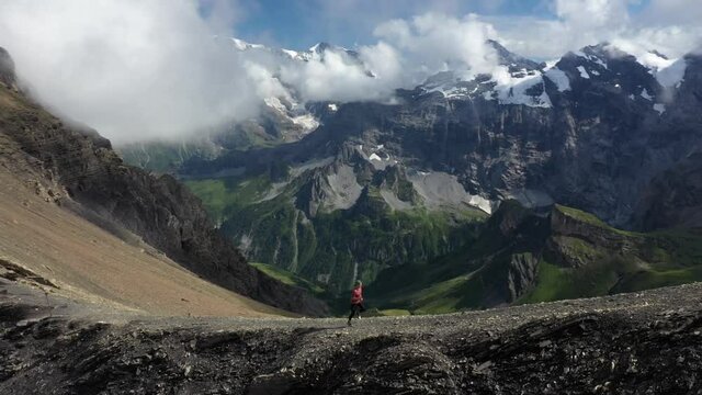 A young and athletic man is running fast up the steep cliff with an amazing and epic landscape with a lush valley in the background. Intense and tough challenge of climbing Schilthorn mountain top.