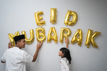 portrait father and daughter muslim decorating eid mubarak letter made of baloon decoration against...