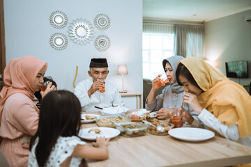 breaking the fast. muslim asian with hijab having iftar dinner together at home sitting on dining table
