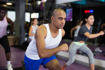 Portrait of young adult man training on step platform at group class in gym