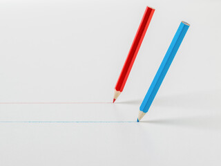 Two colored pencils drawing straight lines on a white background.
