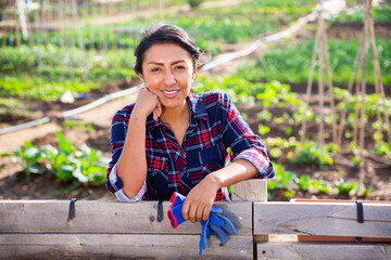 Hardworking woman on farm resting by fence with gloves in hand