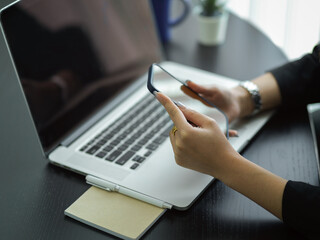 Side view of businesswoman using smartphone while working with laptop