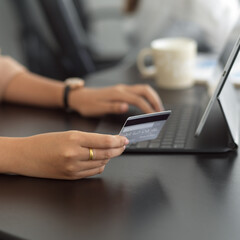 Female hand holding credit card and typing on tablet keyboard in office room