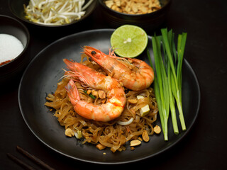 Pad Thai, stir fried Thai noodle with shrimps on black ceramic plate with lime and chives
