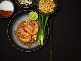 Pad Thai, stir fried Thai noodle with shrimps on black ceramic plate with lime and chives