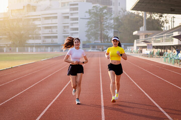 Obraz premium Two young Asian women in sports outfits jogging on running track in city stadium in the sunny morning to keep fitness and healthy lifestyle. Young fitness women run on the stadium track
