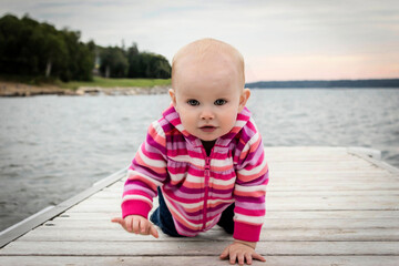 little caucasian baby girl crawling on wooden pier.