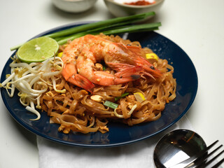 Stir fired Thai noodles with shrimps serving on ceramic plate with lime, beansprouts and chives