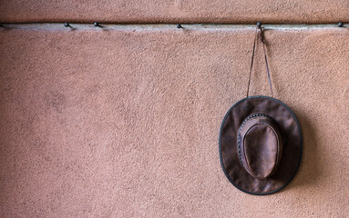 Single leather cowboy hat hanging on a row of steel pegs on an adobe wall