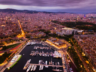 Night aerial view from drones of old port in Barcelona with of sailboats and yachts and gothic quarter, historical part of the city ..
