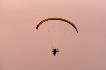 Silhouette of the Paramotor gliding and flying In the air through soft sunlight sky