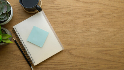 Top view of notebook, pencil, sticky note, coffee cup and copy space on wooden table