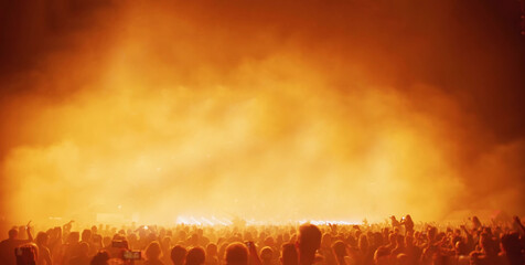 Crowd of people in concert festival against spotlight and smoke.