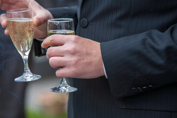 The groom holds a glass or flute of champagne on the background of the friends on nature at the wedding ceremony. Close up. Toast. High quality photo