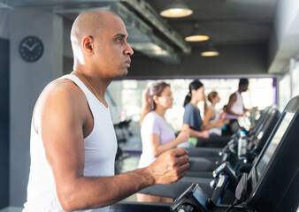 Portrait of sporty young adult man running on treadmill in gym