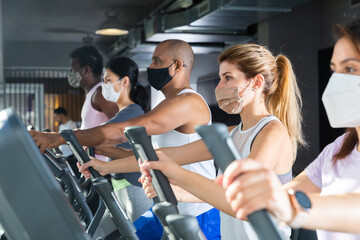 Fototapeta na wymiar Active people in protective masks having running elliptical trainer class in health club
