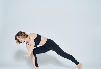 A slender woman in sportswear is engaged in fitness on a light background