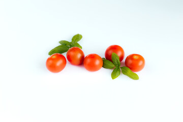 Red cherry tomatoes with green basil on a white background
