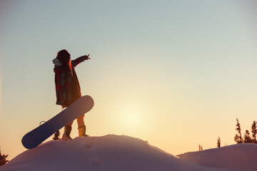 Young girl snowboarder stands at sunset mountain top