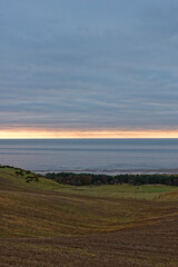 Fototapeta na wymiar The sun rising beneath the Low Cloud layer over Lunan bay and the rolling Farmland behind the beach on an early morning in February.