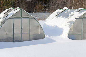 Winter view of two snow-covered greenhouses in the afternoon sun